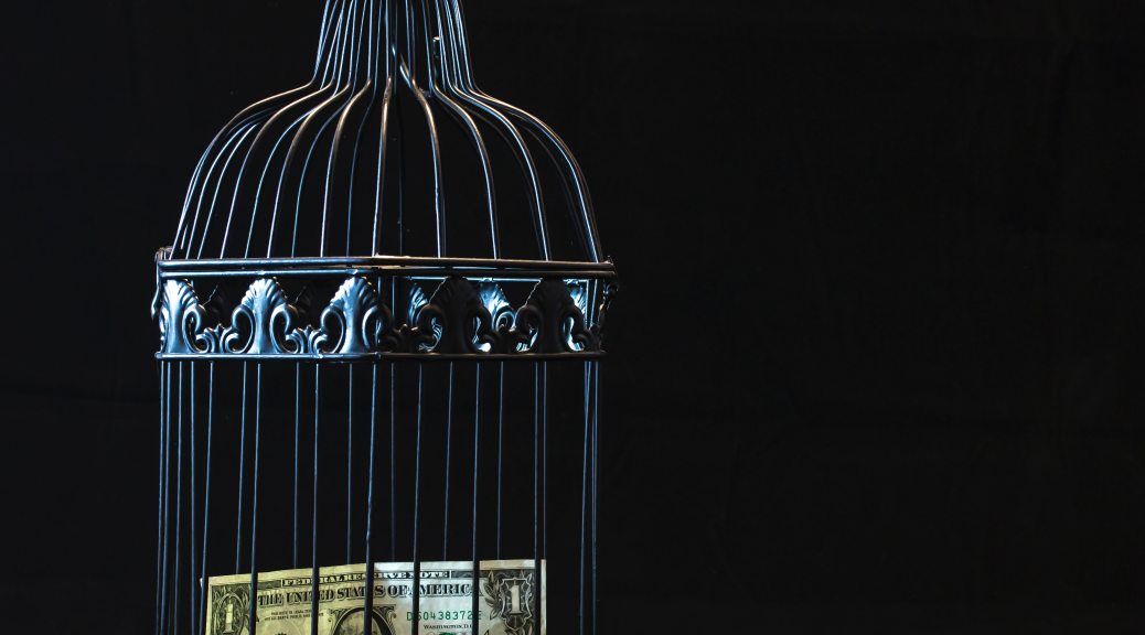 A picture of a small black metal birdcage containing a dollar bill. The image is dark, with blackness surrounding the featured image